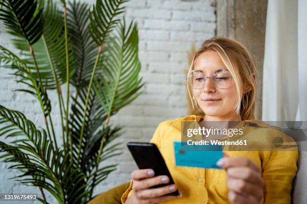 female entrepreneur making online payment through credit card at home - phone payment stock-fotos und bilder