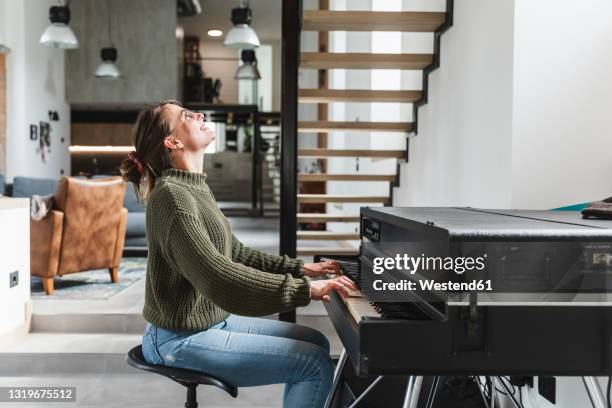 happy woman playing piano in living room at home - klavier stock-fotos und bilder