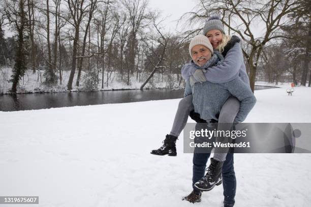 man piggybacking playful woman while standing on snow - sweater weather stock pictures, royalty-free photos & images