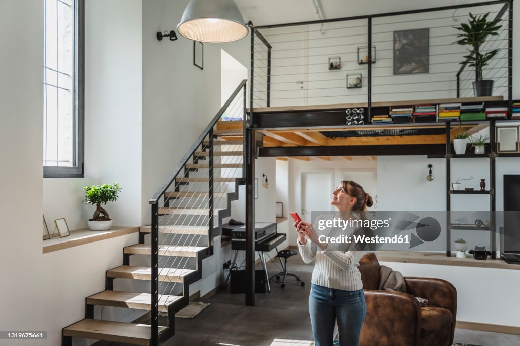 Young woman controlling smart home functions through mobile phone at modern home