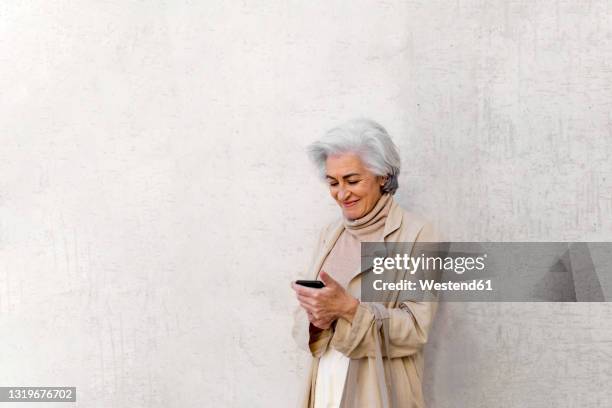 smiling mature woman using mobile phone in front of wall - fashion in an age of technology costume institute gala arrivals stockfoto's en -beelden