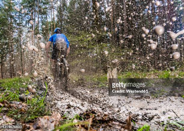 young man riding mountain bike through mud in forest - mud stock-fotos und bilder