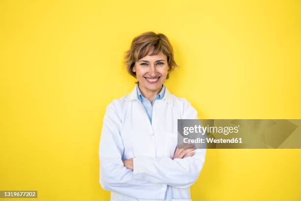 smiling female scientist standing with arms crossed in front of wall - laboratory coat stock-fotos und bilder
