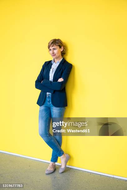 female entrepreneur standing in front of yellow wall - lehnend stock-fotos und bilder