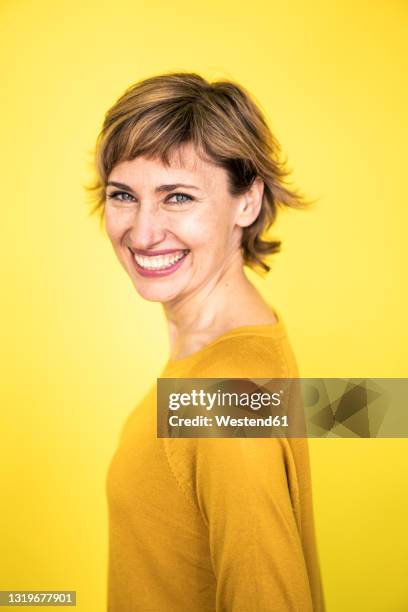 cheerful mature woman standing by yellow background - gelber hintergrund stock-fotos und bilder