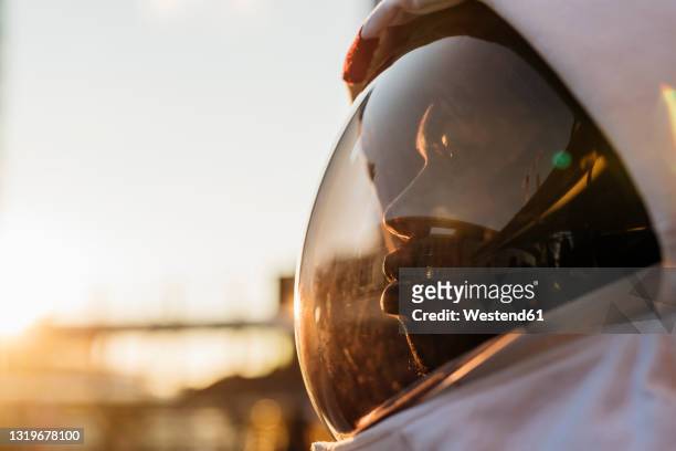 mid adult astronaut wearing space helmet looking away during sunset - astronaut helm stock-fotos und bilder