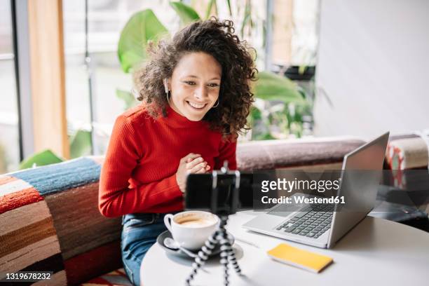 young influencer with hands clasped vlogging through smart phone at cafe - stream fotografías e imágenes de stock