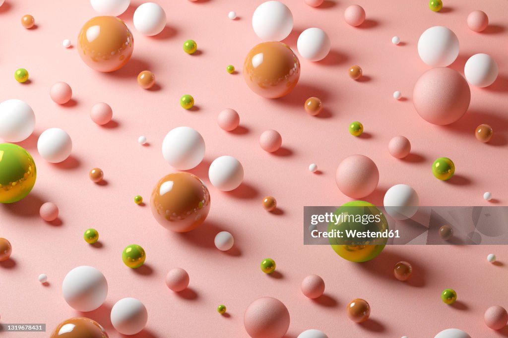 Three dimensional pattern of various spheres flat laid against pink background