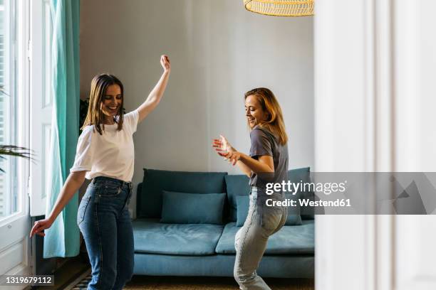 happy girlfriends dancing in living room at home - girlfriend stock-fotos und bilder