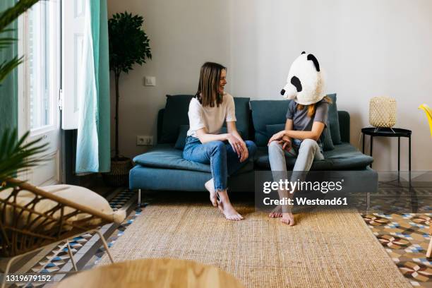 smiling woman looking at girlfriend wearing panda mask in living room - weird roommate stock pictures, royalty-free photos & images