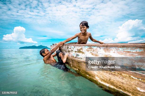 bajau children pulling each other up a wooden canoe - pacific islands stock pictures, royalty-free photos & images