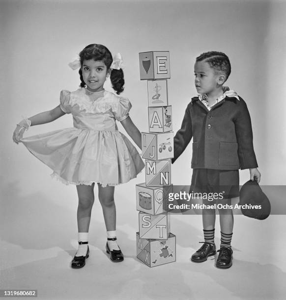 Studio portrait of a young boy and girl, both smartly dressed, as they play with building blocks, against a neutral background, location unspecified,...