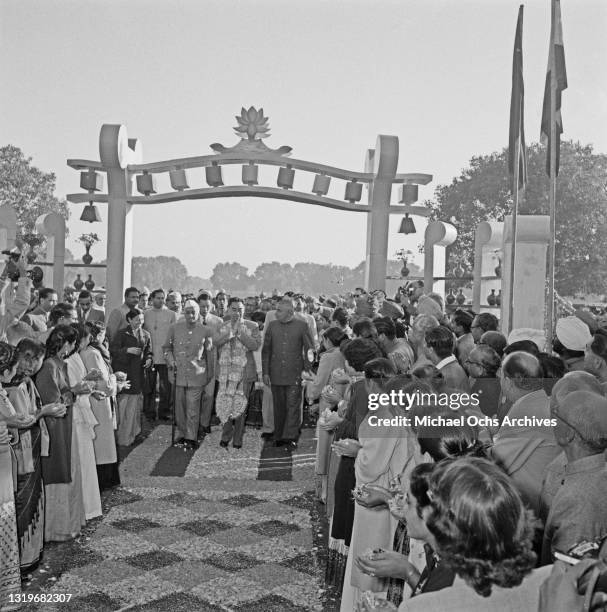 Premier of the People's Republic of China Zhou Enlai passes beneath an arch, rose and jasmine petals strewn across the floor, his hands together,...