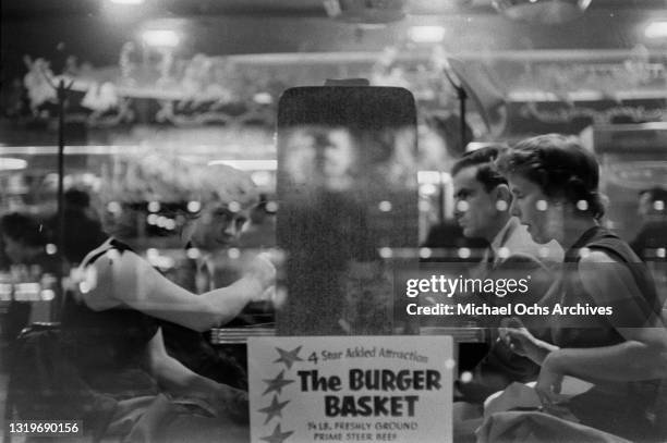 Two couples sit at a table in a diner, a sign on the window reads '4 star added attraction, The Burger Basket, 1/4 lb freshly ground prime steer...