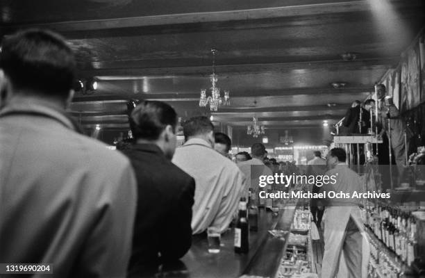 Drinkers rest their elbows against the bar, while bartenders on the other side take the orders, at an unspecified nightclub in New York City, New...