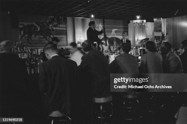 An unspecified piano trio, the drinkers at the bar obscuring the pianist, performing at an unspecified nightclub in New York City, New York, circa...