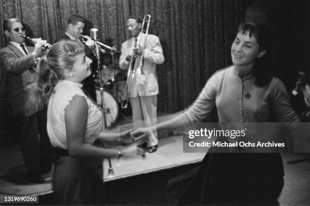 Two young women dancing as an unspecified jazz band, with a clarinettist, trumpeter, trombonist and drummer visible, performs at an unspecified...