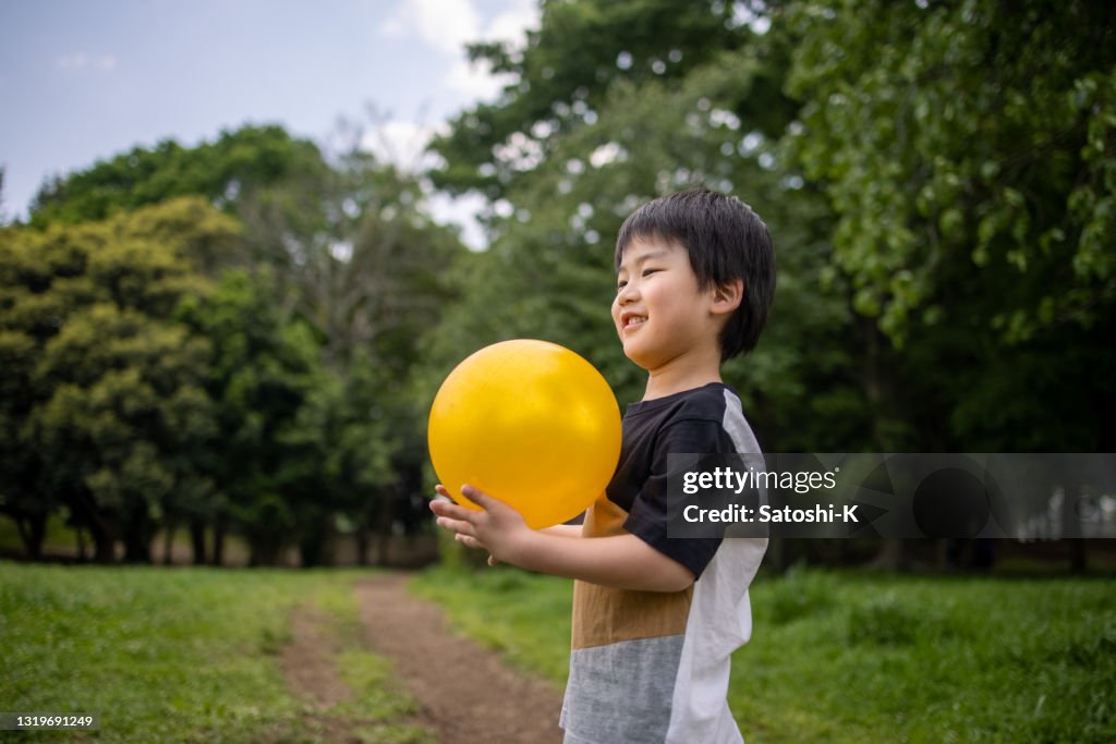 公共の公園で黄色いボールを持っている小さな男の子