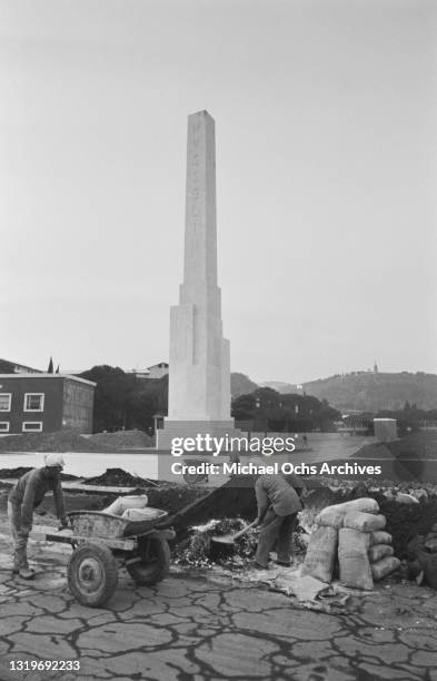 Construction workers with wheelbarrows working before the Stele Mussolini, a Carrara marble obelisk measuring over 17 metres tall, on the Foro...