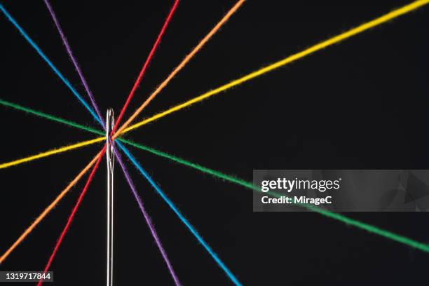 rainbow colored threads through needle eyelet - einfädeln stock-fotos und bilder