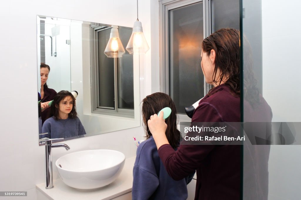 Mother brushing and drying daughters hair in home bathroom