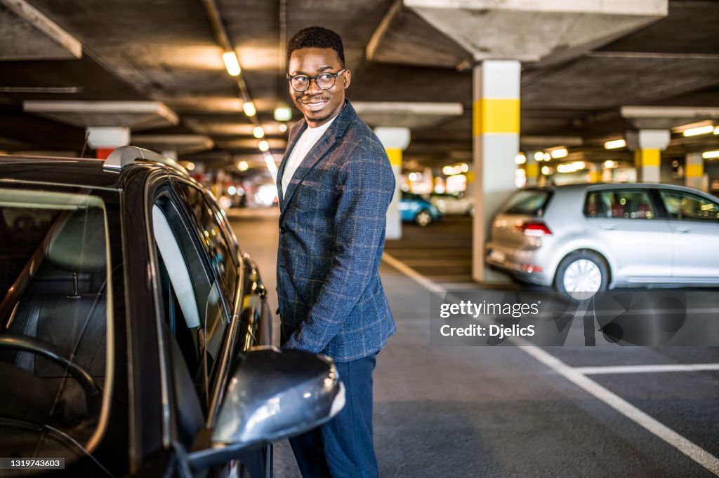 Happy businessman entering his car at car parking garage.