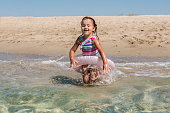 Happy cute tollder girl  in swimsuit with swim tubes ring going into the sea for swimming on sunny day. Kids having fun at the beach. Family vacation with children concept