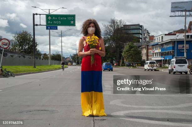 Woman stands in the middle of the road with a dress with the Colombian flag colors upside down and flowers as Bogota, Colombia enters its third week...