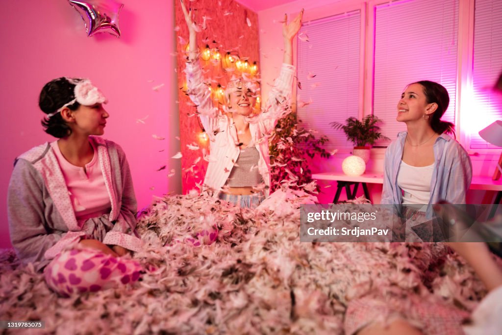 Young women having fun at a slumber party with flying feathers