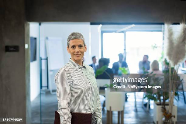 retrato de una empresaria sonriente trabajando en una oficina moderna ocupada - accionista fotografías e imágenes de stock