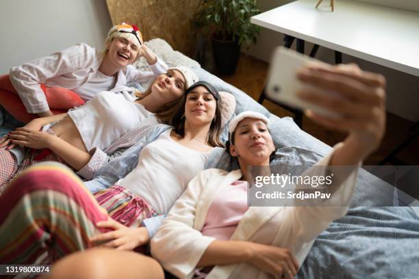 hochwinkelansicht glücklicher junger frauen, die selfies machen, während sie zusammen im bett liegen - übernachtungsparty stock-fotos und bilder