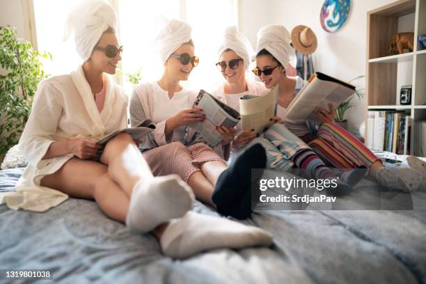 low-angle view of four female friends enjoying reading beauty magazines together - magazine party stock pictures, royalty-free photos & images