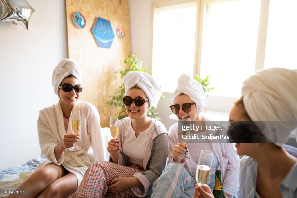 Lächelnde junge Frauen reden und trinken Champagner auf einer Schlummerparty