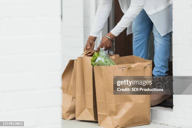 senior adult woman picks up grocery order from front stoop - grocery delivery stock pictures, royalty-free photos & images