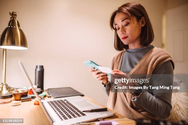 young pretty asian woman checking her medical insurance card while making telemedicine appointment on smartphone at home - medical insurance stock-fotos und bilder