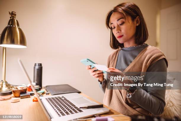young pretty asian woman checking her medical insurance card while making telemedicine appointment on smartphone at home - medical insurance stock pictures, royalty-free photos & images