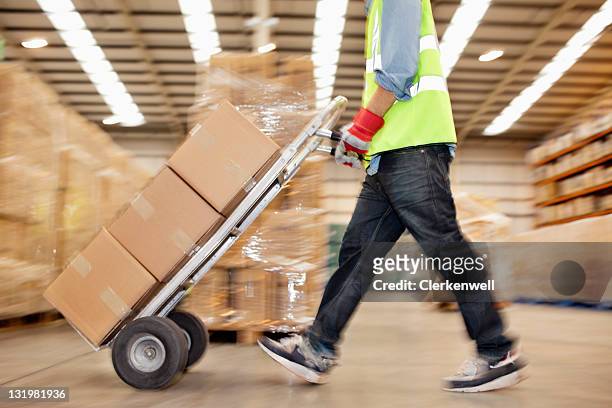 side view of worker pushing trolley of cardboard boxes through warehouse - pushing stock pictures, royalty-free photos & images