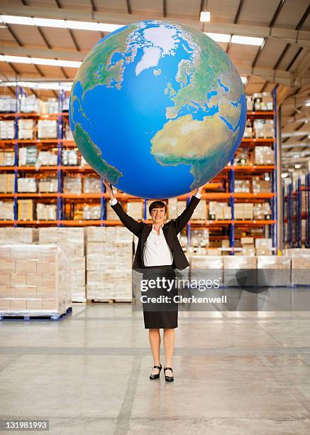 mature woman holding aloft a large blue ball in warehouse - big world stock pictures, royalty-free photos & images