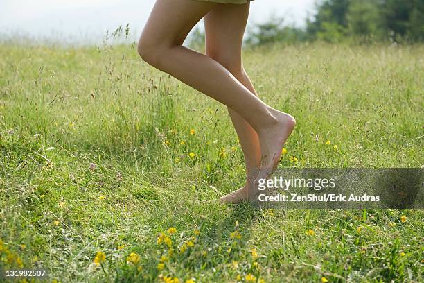 woman walking on meadow with bare feet, low section - legs walking stock-fotos und bilder