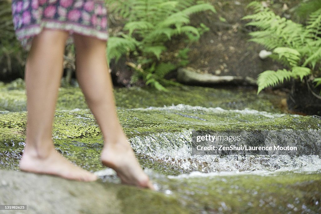 Young woman dipping toes in stream, cropped