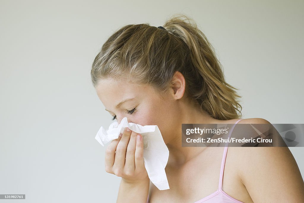 Young woman sneezing into tissue