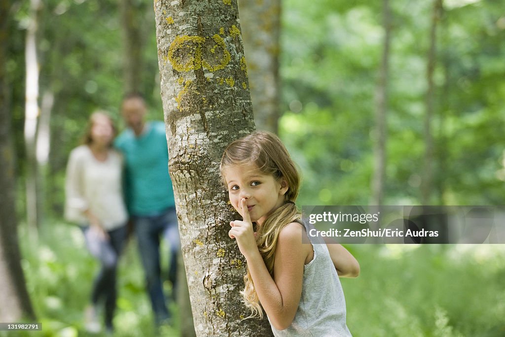 Girl hiding behind tree with finger on lips