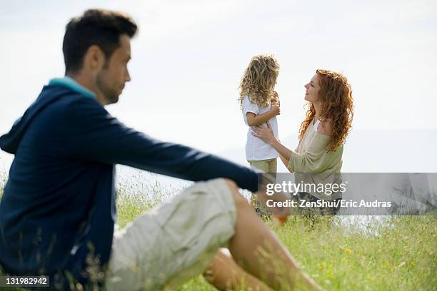 mother talking with young daughter outdoors, father watching from foreground - family law stockfoto's en -beelden