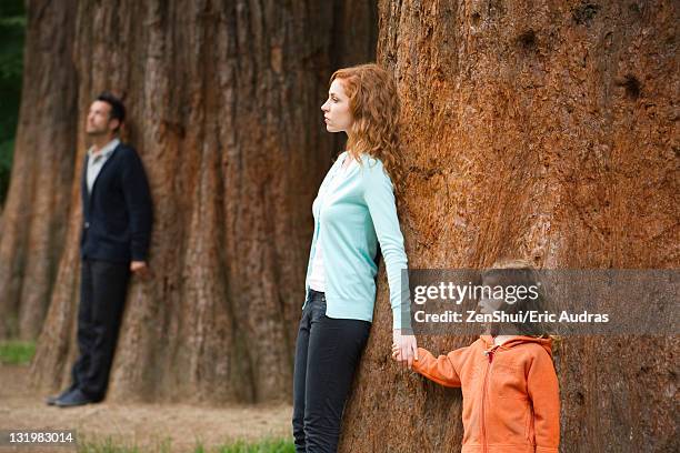 mother and daughter leaning against tree, father standing separate in background - divorce kids fotografías e imágenes de stock