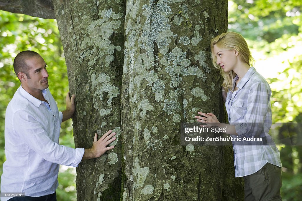 Couple looking at each other around tree trunks