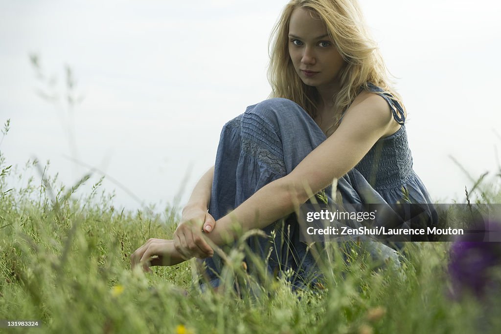 Young woman sitting in field of grass, portrait