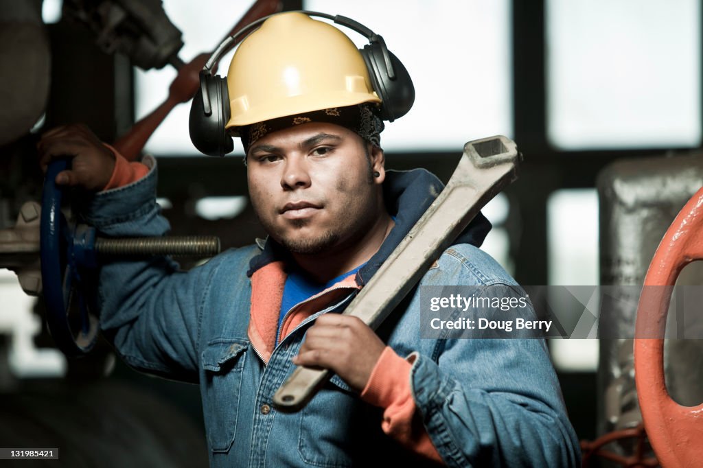 Mixed race worker in hard-hat holding large wrench