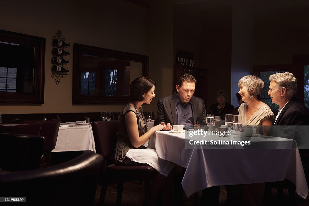 Friends watching man blow out birthday cupcake in restaurant