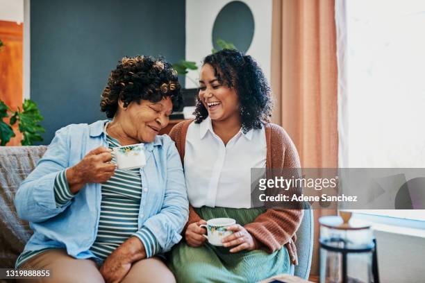 自宅のソファで高齢の親戚とコーヒーを飲む若い女性のショット - mom and young daughter ストックフォトと画像