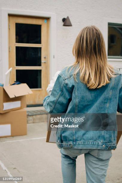 rear view of young blond woman carrying box at back yard - chaqueta tejana fotografías e imágenes de stock
